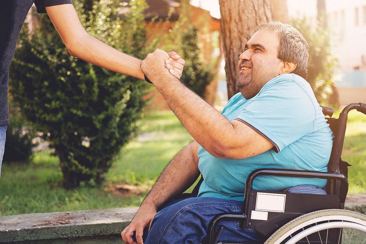 Friends meeting in the park and doing handshake, one main in wheelchair