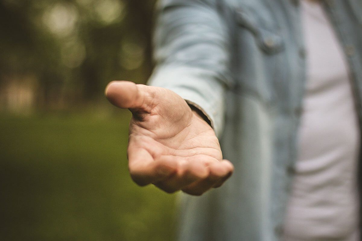 Young man in standing in park stretches his hand. Focus is on hand. Close up.