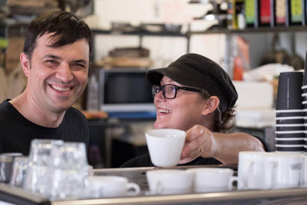 Nundah Community Enterprise Co-operative staff smiling over coffee machine at cafe