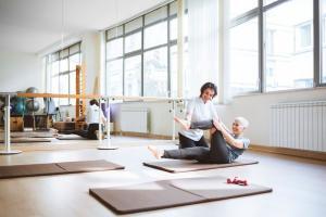 Senior woman doing fitness exercise on mat with her instructor helping.