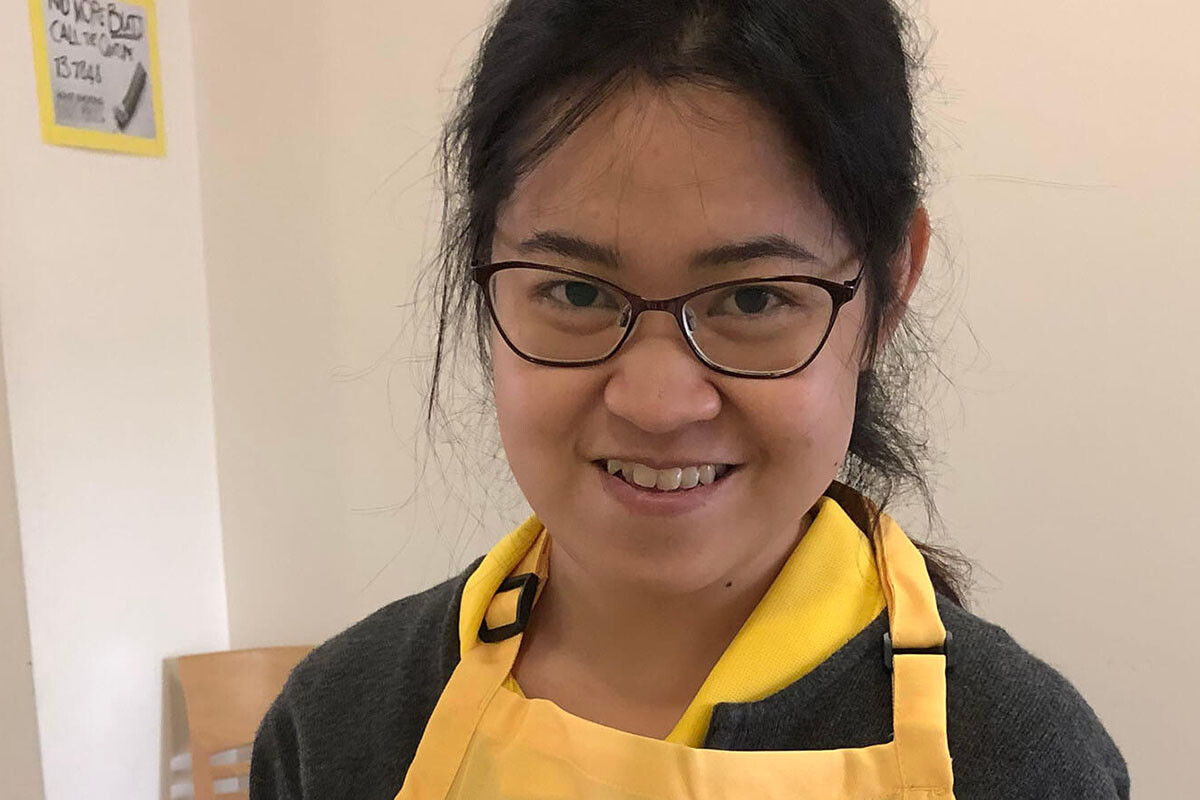 RAC's Jenelle organsing flowers, smiling at camera in yellow apron