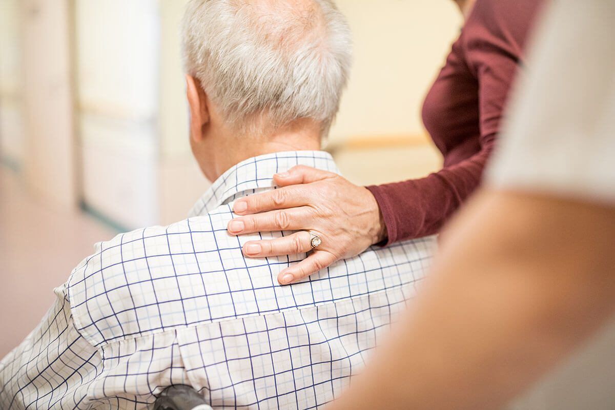 Disabled man with wife in hospital. Senior man on wheelchair pushed by nurse.