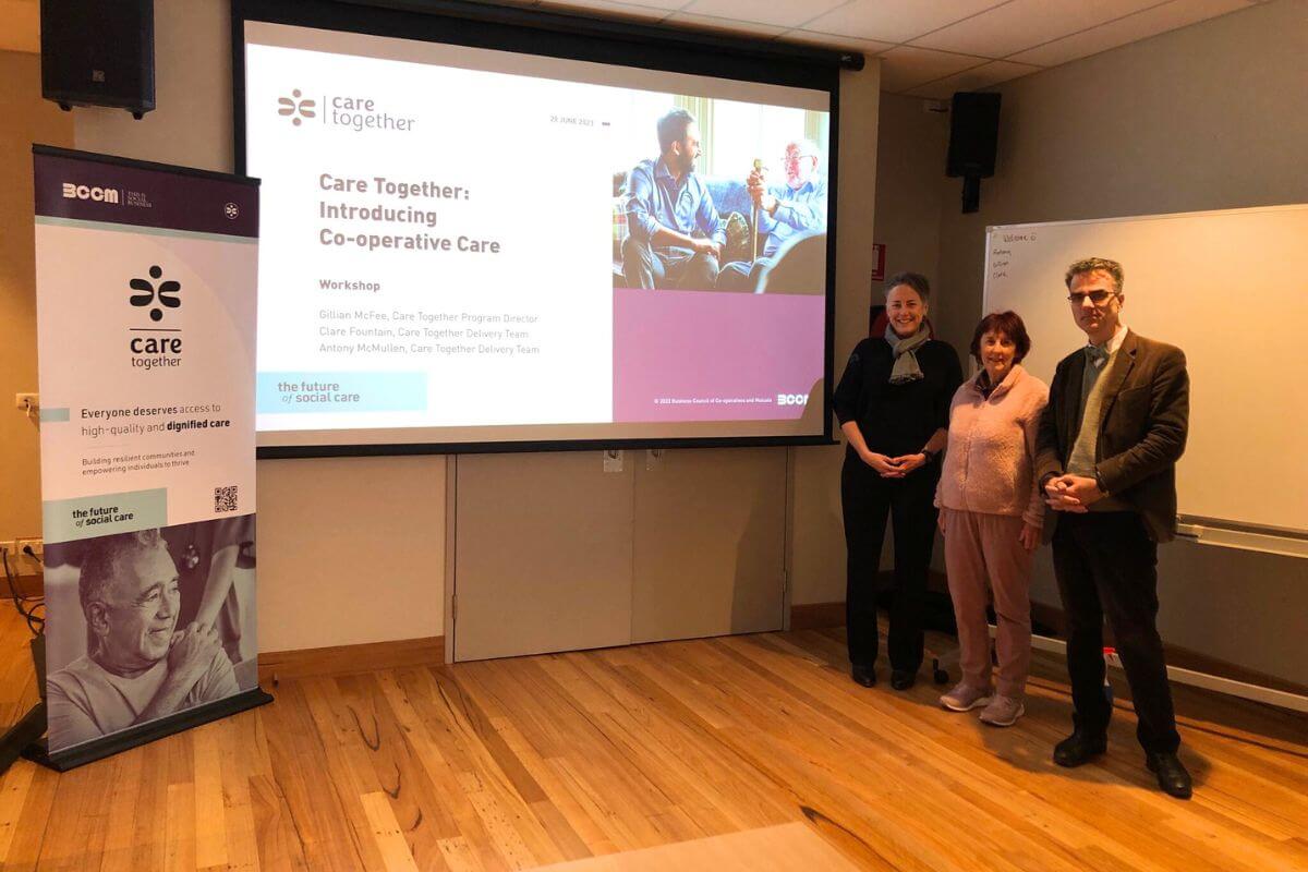 Clare Fountain, Gillian McFee and Antony McMullen ready to present Care Together's Introducing Co-operative Care workshop Bega June 2023. They are standing in front of the presentation screen and banner.